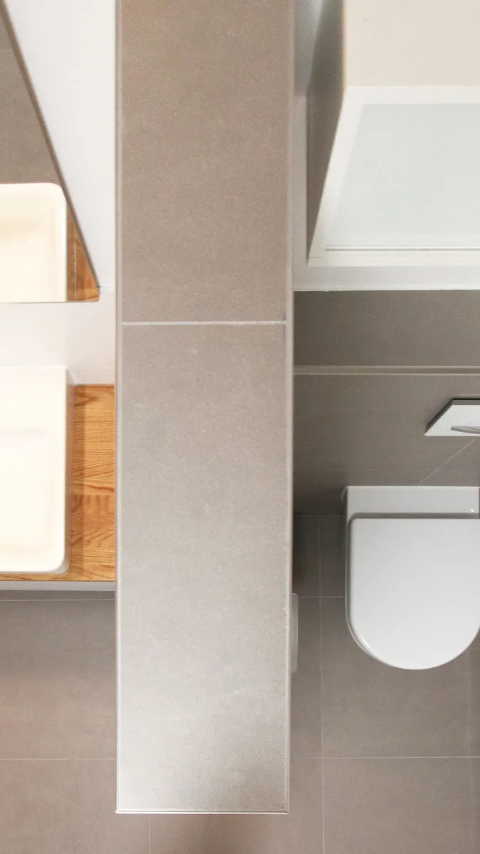 Modernes Badezimmer aus der Vogelperspektive, mit Fokus auf den Waschtisch, einem vertikal angeordneten Schrank und einer minimalistischen WC-Anlage. Dezente Farben und klare Linien schaffen eine elegante Atmosphäre.