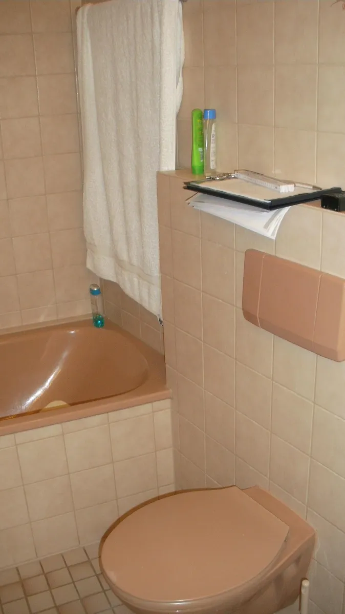 Ein Badezimmer im Retro-Stil mit beigefarbenen Fliesen und sanitären Einrichtungen in passender Farbe.