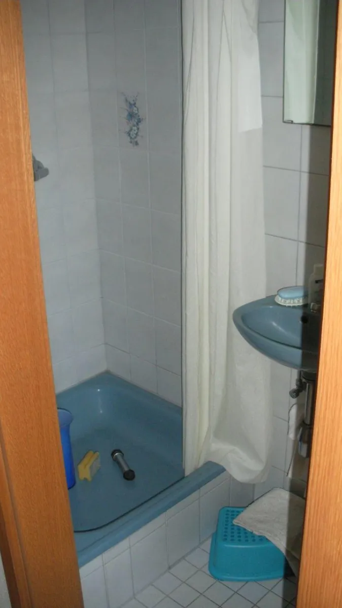 Ein kleines Badezimmer mit einer blauen Duschwanne, die von weißen Fliesen umgeben ist, teilweise mit floralen Motiven verziert. 