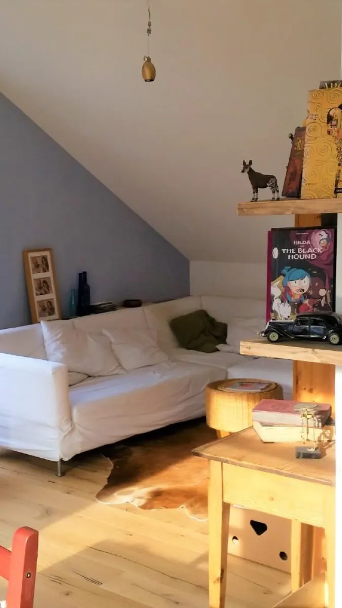 Ein gemütliches Wohnzimmer in einer Dachgeschosswohnung mit einer weißen Eckcouch, die an einer blauen Wand steht. 