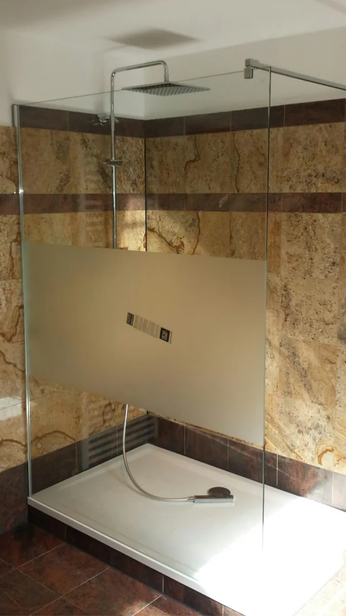 Eine geräumige, bodengleiche Dusche mit einer Glasabtrennung, die teilweise mattiert ist, steht in einem Badezimmer mit Naturstein-Wänden. 