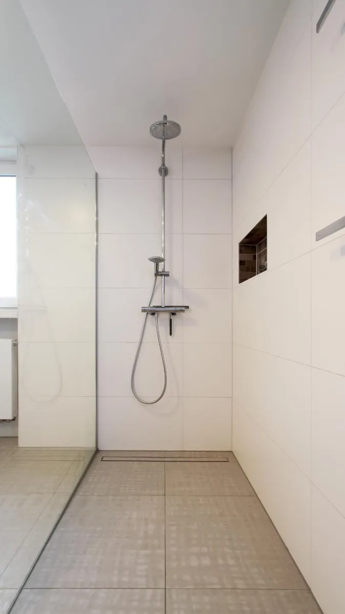 Eine moderne, ebenerdige Dusche mit minimalistischem Design und einer Regenbrause aus Edelstahl.