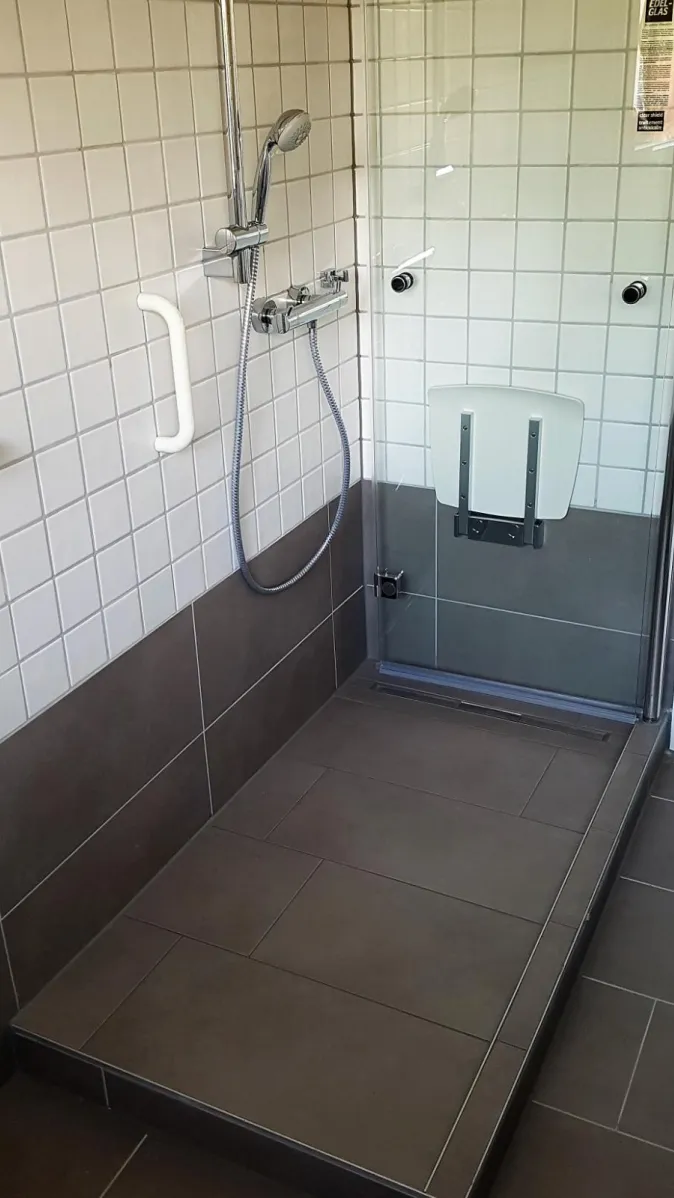 Eine bodengleiche Dusche mit dunklen, großformatigen Fliesen und einer Duschabtrennung aus Glas.