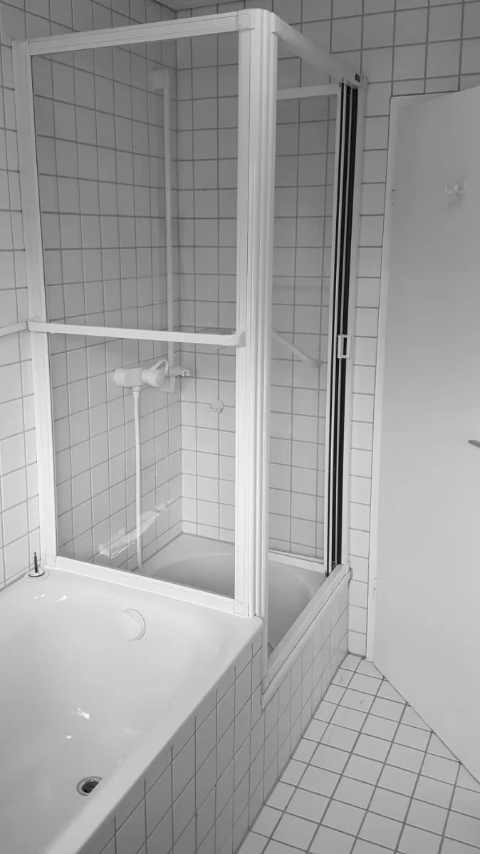 Ein Badezimmer mit einer kombinierten Badewanne und Duschkabine, die von einem weißen Rahmen und klarem Glas eingefasst ist.