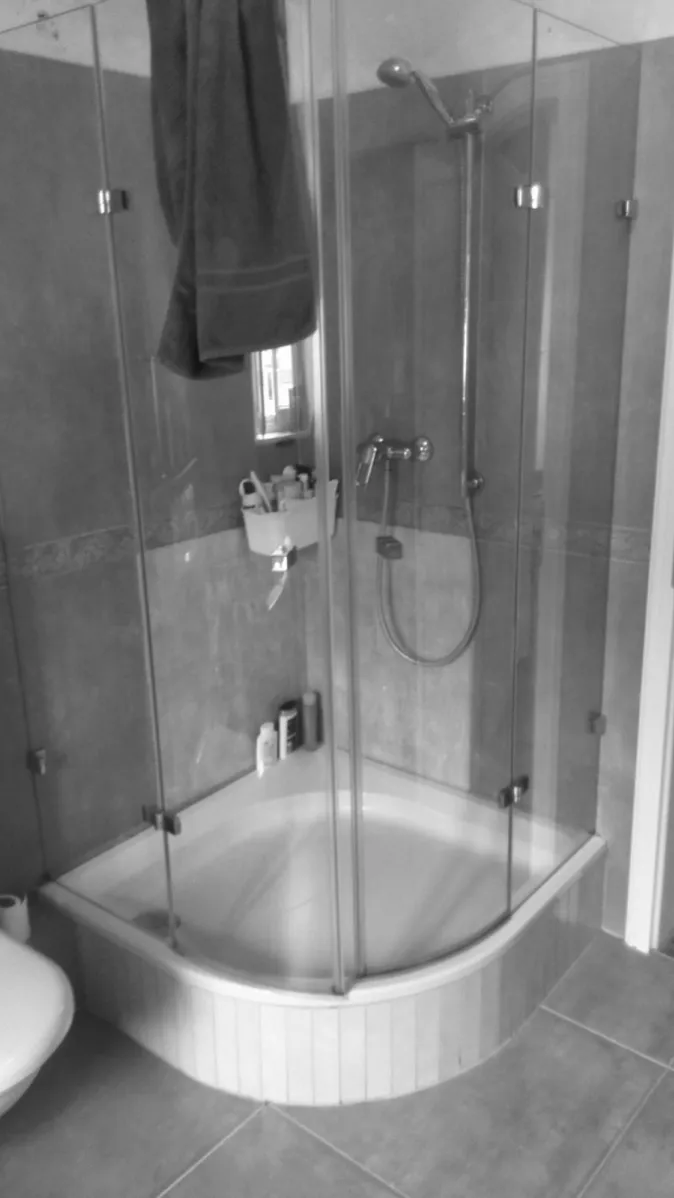 Eine Eckdusche mit gebogener Glastür und einer weißen Duschwanne, eingebaut in ein Badezimmer mit Fliesenwänden in natürlichem Beige.