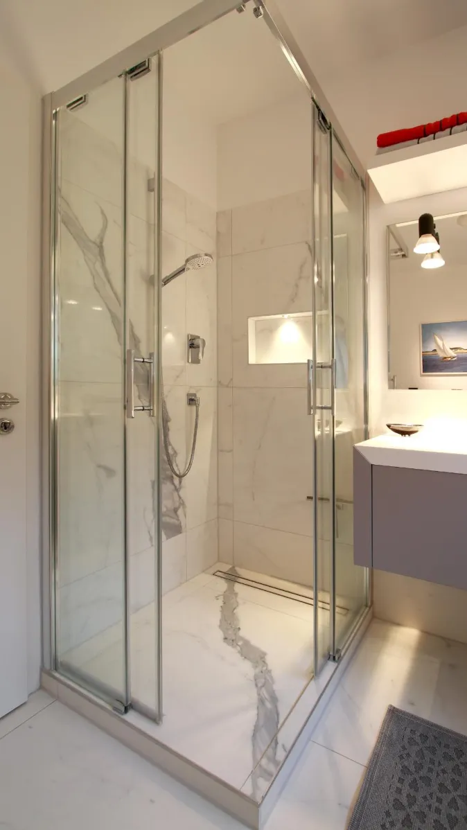 Eine luxuriöse Duschkabine mit Marmoreffekt-Fliesen und einer Schiebetür aus klarem Glas.
