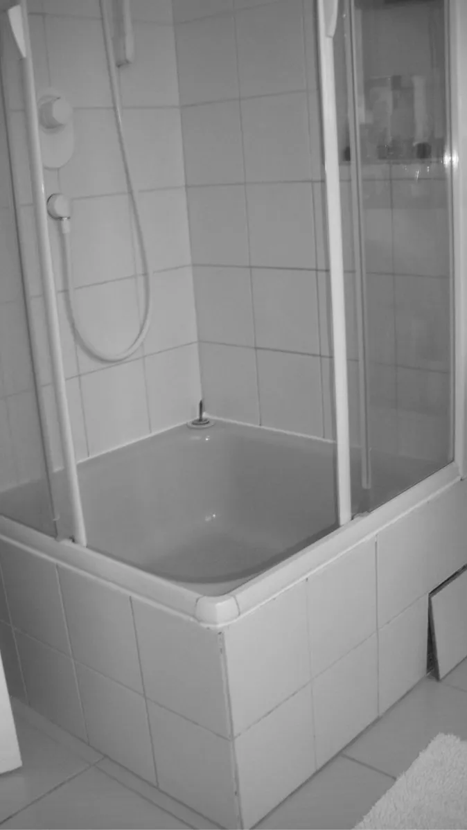 Ein kleines Badezimmer mit einer erhöhten Duschwanne, die von weißen Kacheln umgeben ist. 