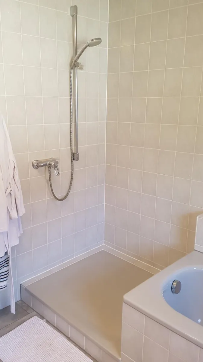 Ein hell gefliestes Badezimmer mit einer offenen Dusche und einer grauen Duschwanne.