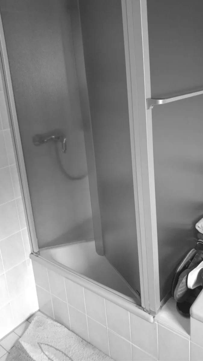 Eine Dusche mit einer matten Glas-Schiebetür, die in einem gefliesten Badezimmer eingebettet ist.