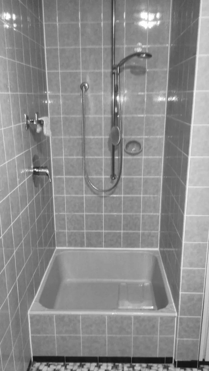 Eine klassische Dusche mit einer niedrigen Duschtasse und vollständig gefliesten Wänden in hellen Tönen.