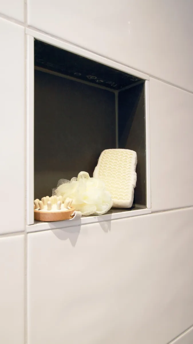 Eine Wandnische in einer Dusche, gefliest mit glänzend weißen Fliesen, enthält praktische Badutensilien.