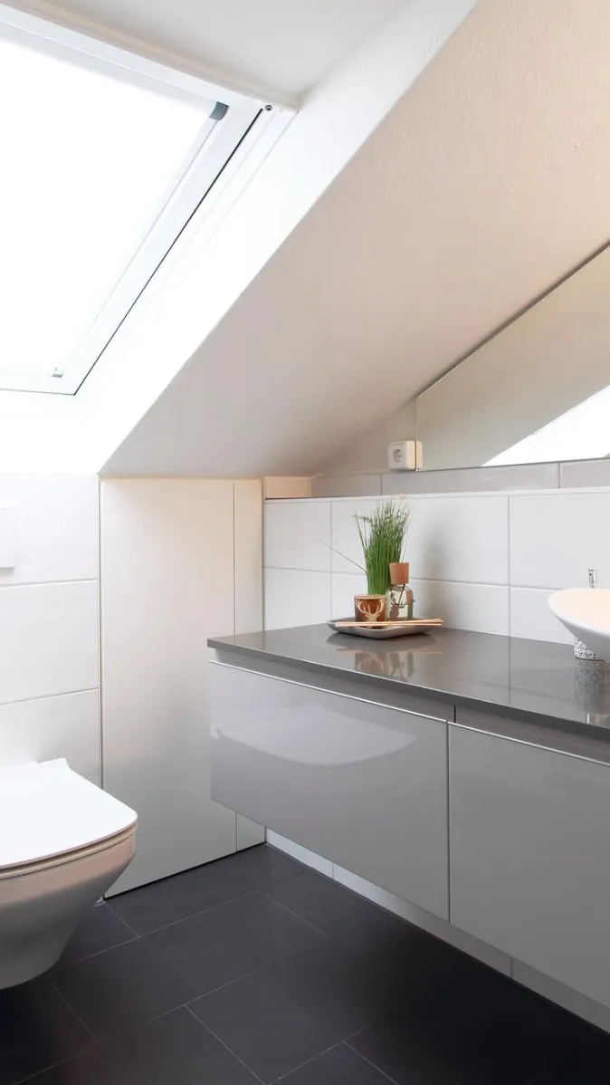 Ein modernes Badezimmer unter einer Dachschräge mit einem großen Dachfenster, das den Raum in natürliches Licht taucht.