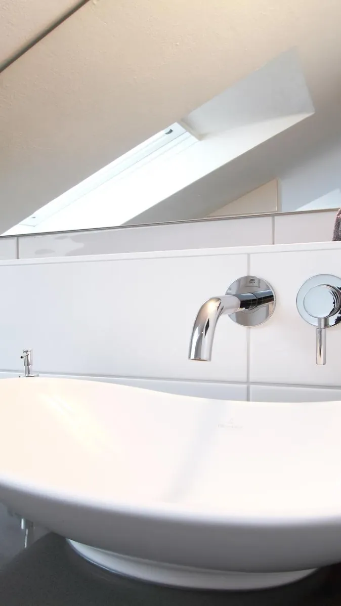 Ein modernes Badezimmer mit einem weißen, ovalen Aufsatzwaschbecken auf einer dunklen, glänzenden Ablagefläche.