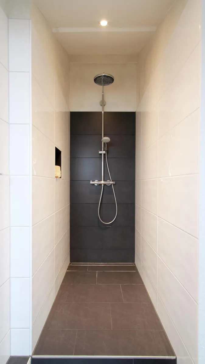 Ein moderner, offener Duschbereich mit weißen Wandfliesen und einer schwarzen Rückwand, die die verchromte Regendusche und Handbrause betont.