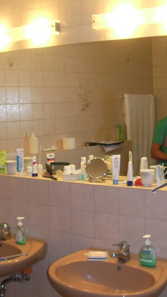 Ein Badezimmer mit beigefarbenen Fliesen, einem großen Wandspiegel und zwei Waschbecken in passender Farbe. 