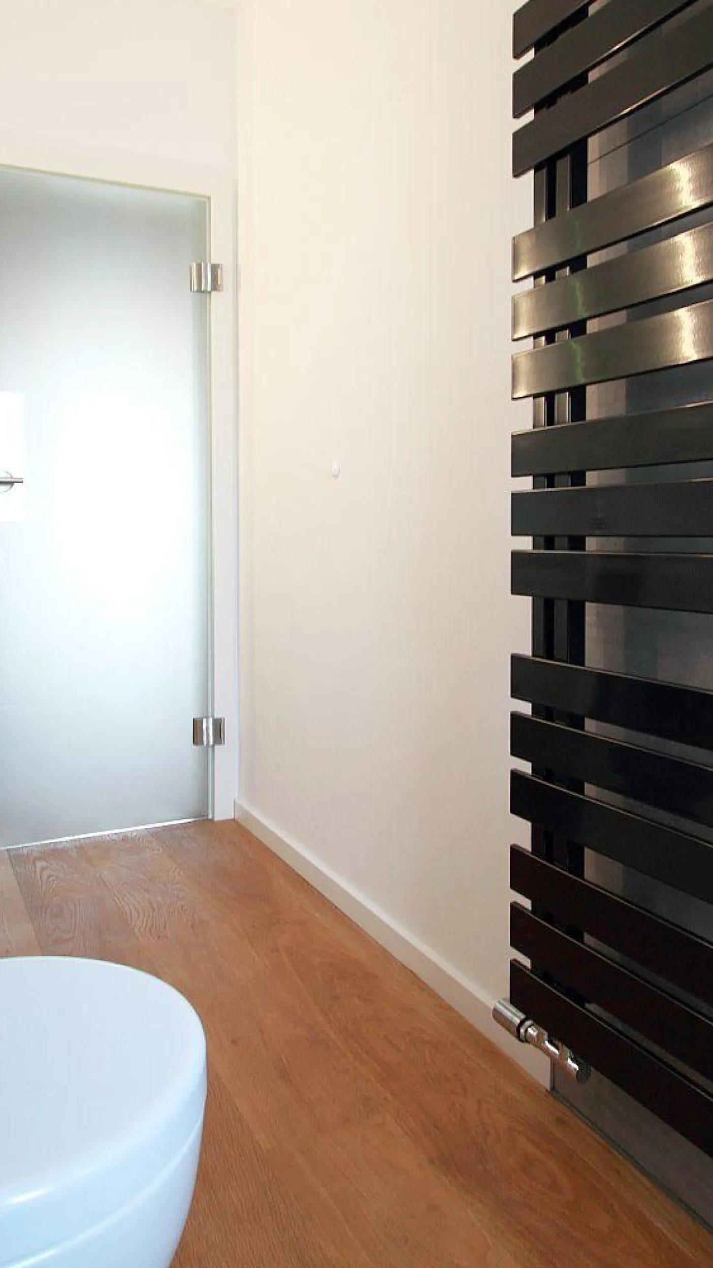 Ein modernes Badezimmer mit einem auffälligen schwarzen Handtuchheizkörper, der sich an der rechten Wand befindet.