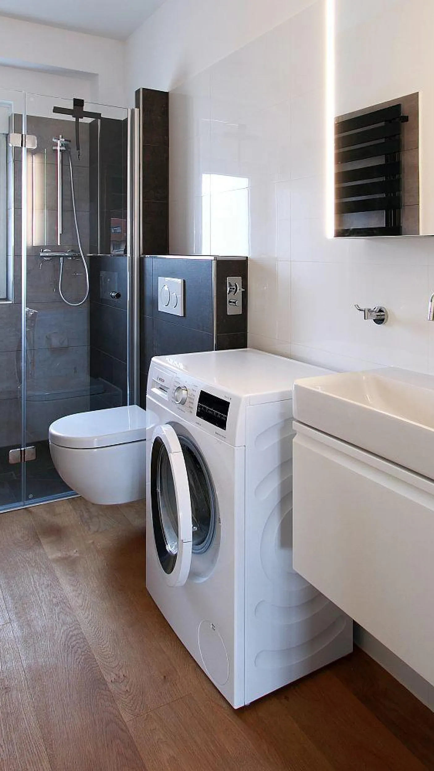 Ein modernes, kompaktes Badezimmer mit einer gläsernen Dusche, einer wandhängenden Toilette und einer Waschmaschine.