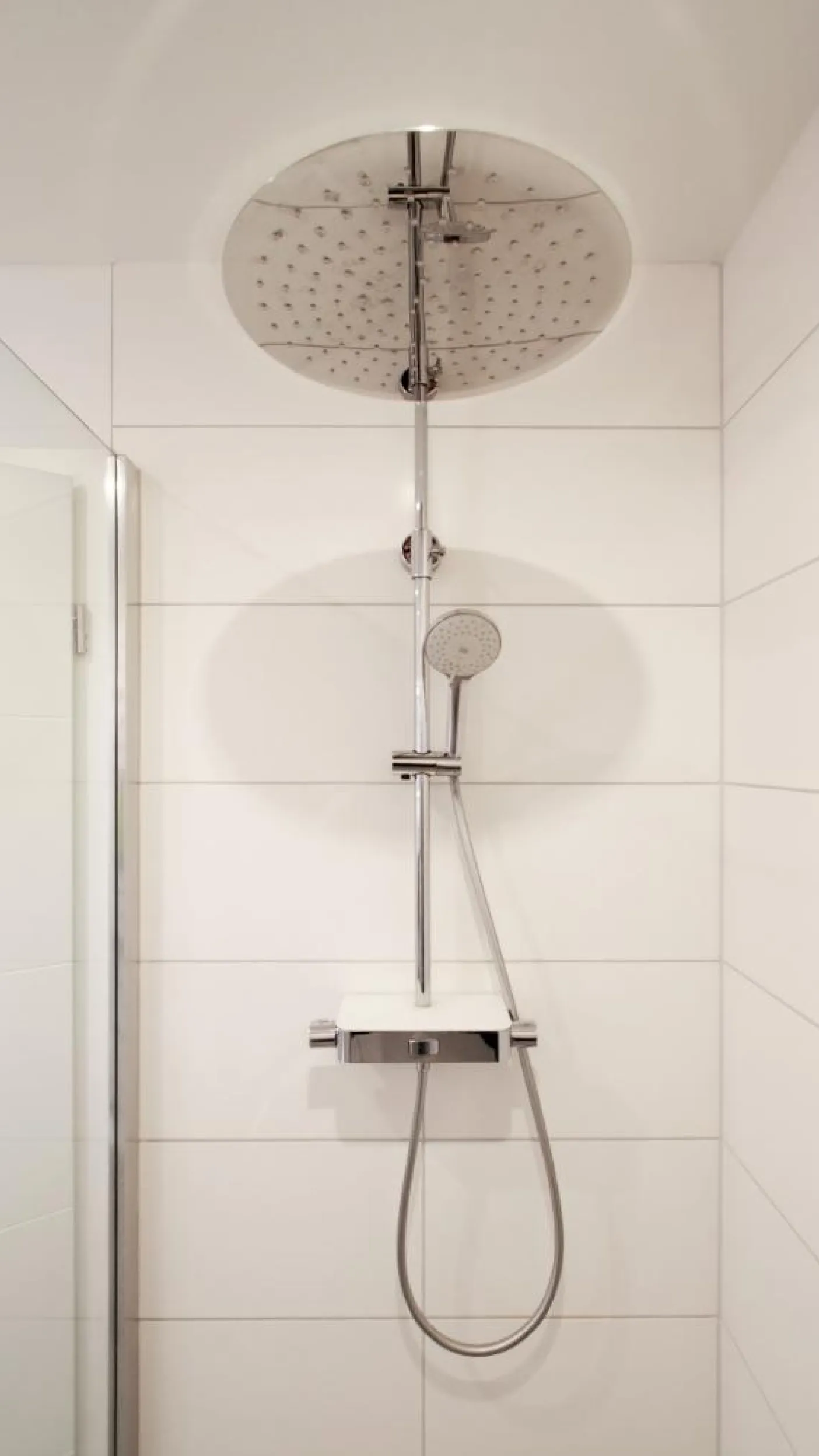 Moderne Dusche mit einer großen runden Regendusche und einer zusätzlichen Handbrause, beide in glänzendem Chrom. 