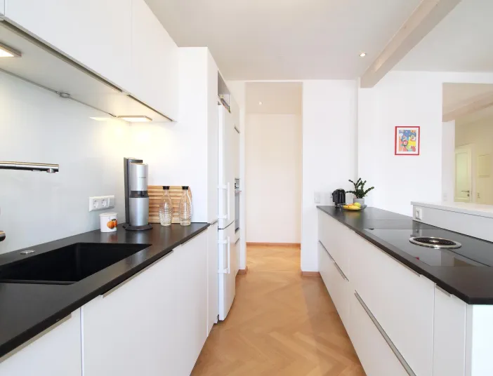 Moderne Küche mit weißen Schränken, schwarzen Arbeitsflächen, eingebautem Waschbecken und Kochfeld. 