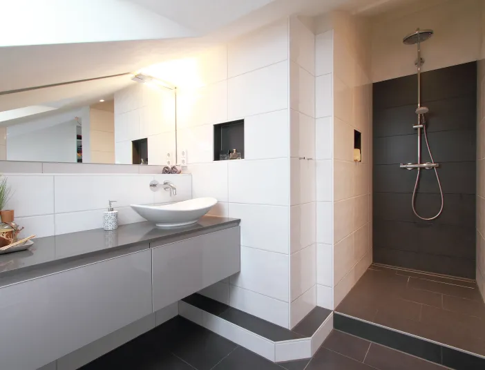 Ein modernes Badezimmer mit einer begehbaren Dusche, die durch dunkle Fliesen hervorgehoben wird und eine Regendusche sowie eine Handbrause bietet.