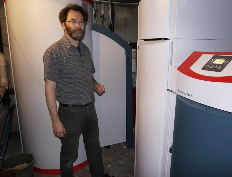 Ein Mann steht in einem Heizungskeller vor einer modernen Heizungsanlage mit einem SolvisLino 3 Heizkessel und einem großen Warmwasserspeicher.