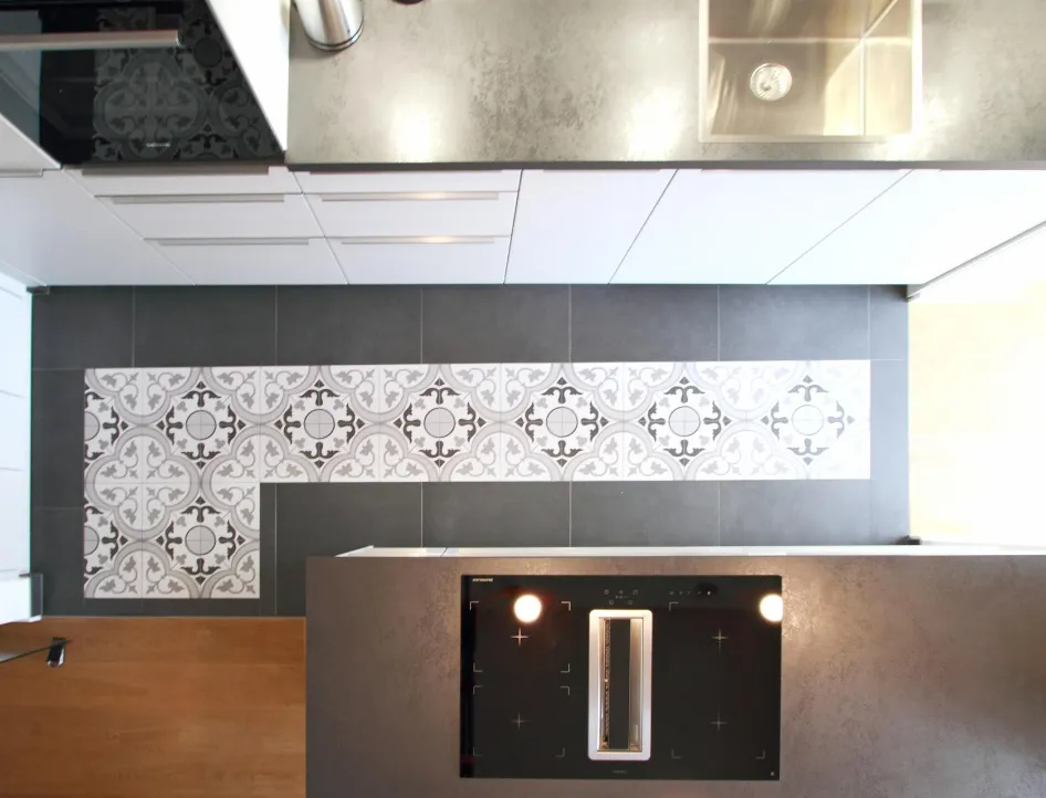 Detailansicht einer modernen Küchenzeile mit stilvollen Fliesen im Vintage-Design. Die Kombination aus grauen Fliesen, einer hochwertigen Arbeitsplatte und einem integrierten Induktionskochfeld verleiht der Küche eine elegante und funktionale Atmosphäre.