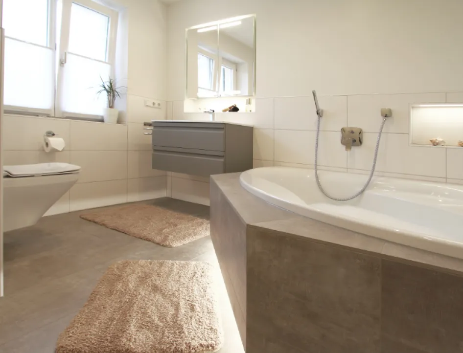 Modernes Badezimmer mit großer Eckbadewanne, wandhängendem Waschtisch und WC, sowie harmonischen Erdtönen und eingebauten Lichtnischen für eine angenehme Atmosphäre.