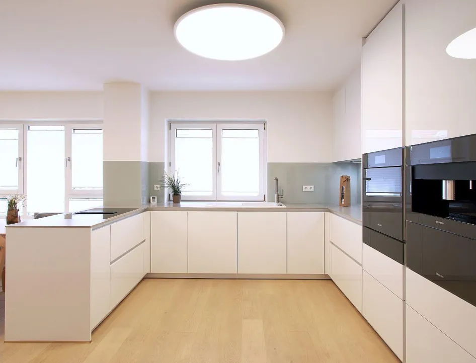 Eine moderne Einbauküche mit weißen, grifflosen Fronten und einer Arbeitsplatte aus grauem Material.