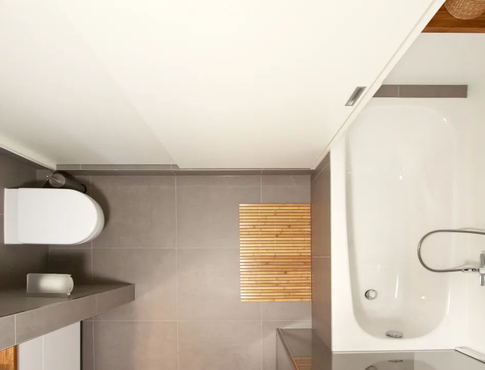 Badezimmer mit Badewanne und WC, aufgenommen aus der Vogelperspektive. Dezente graue Fliesen, ein heller Holzbodenmatten-Akzent und klare Linien schaffen eine moderne und schlichte Atmosphäre.