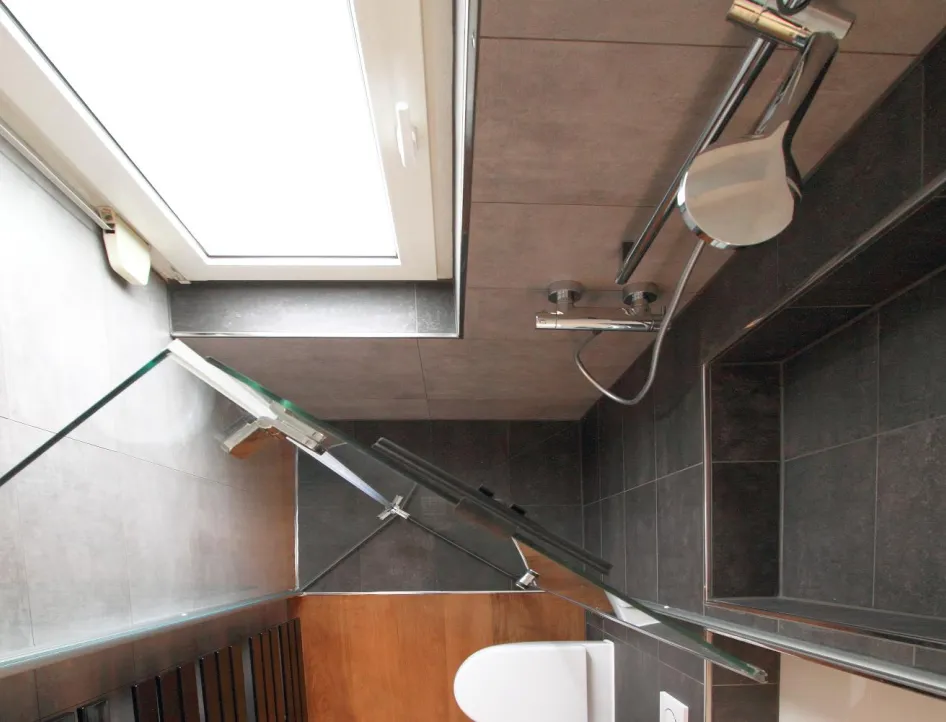 Ein kleines Badezimmer mit Dachschräge, in dem dunkle Fliesen an Wänden und Decke für eine moderne Optik sorgen.