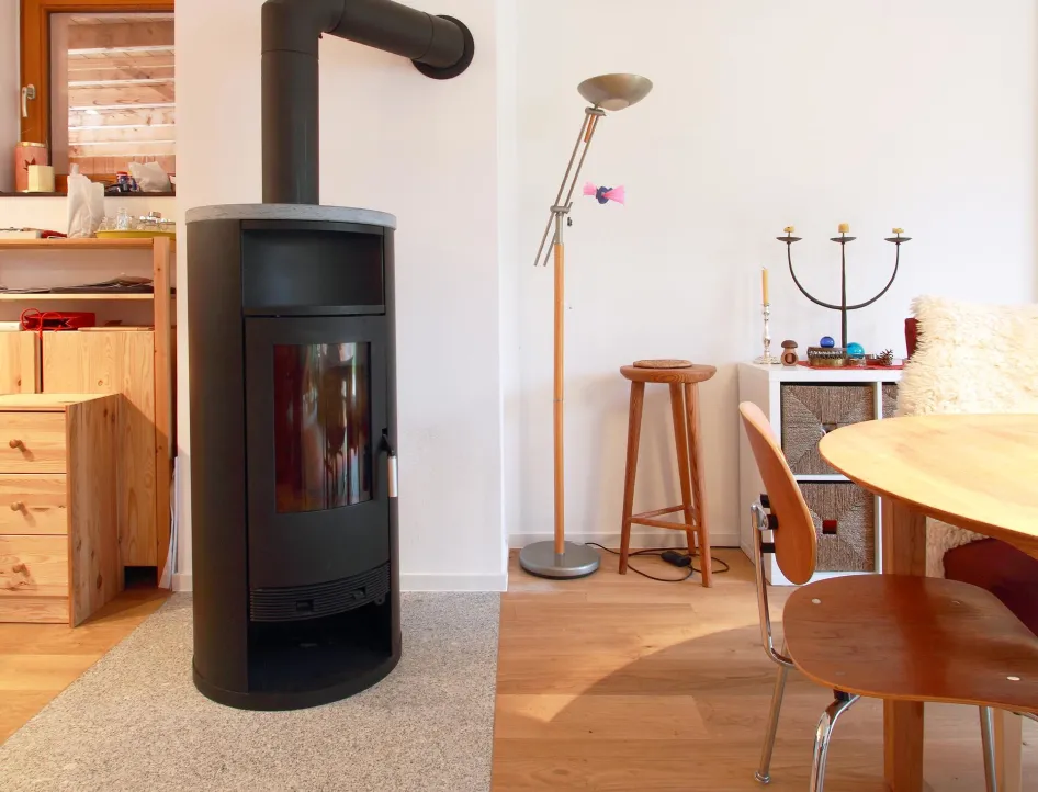 Ein gemütlicher Wohnbereich mit einem modernen schwarzen Kaminofen, der auf einer grauen Schutzmatte steht. 