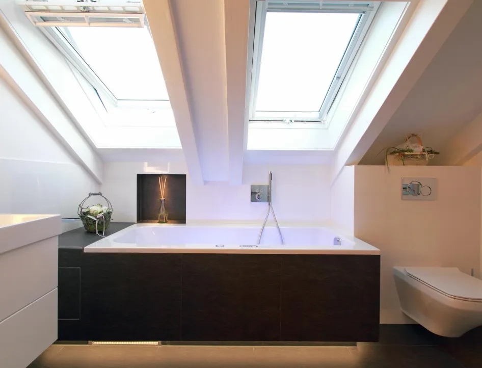 Ein stilvolles Badezimmer unter einer Dachschräge mit zwei großen Dachfenstern, die den Raum mit Tageslicht erhellen.