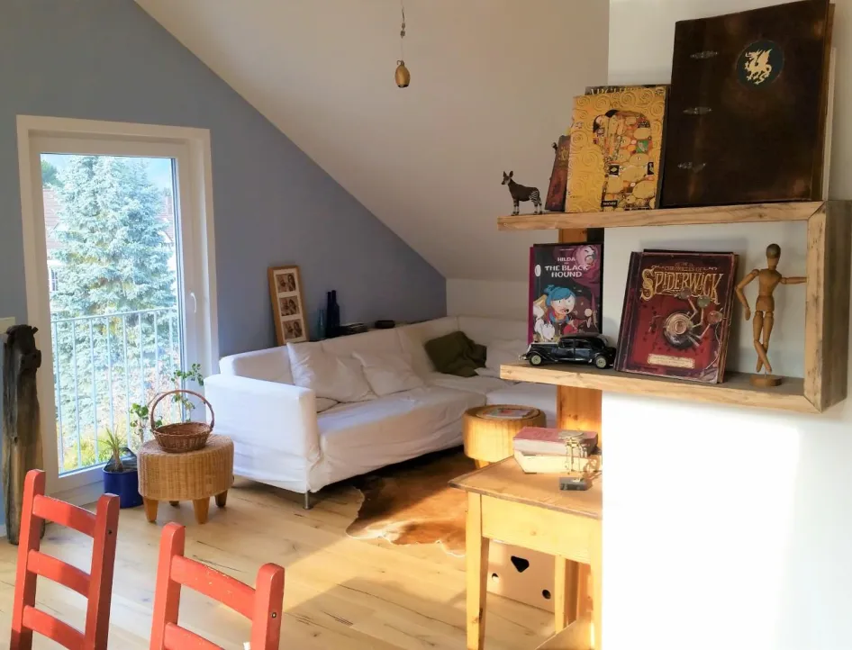 Ein gemütliches Wohnzimmer in einer Dachgeschosswohnung mit einer weißen Eckcouch und einer blauen Akzentwand.