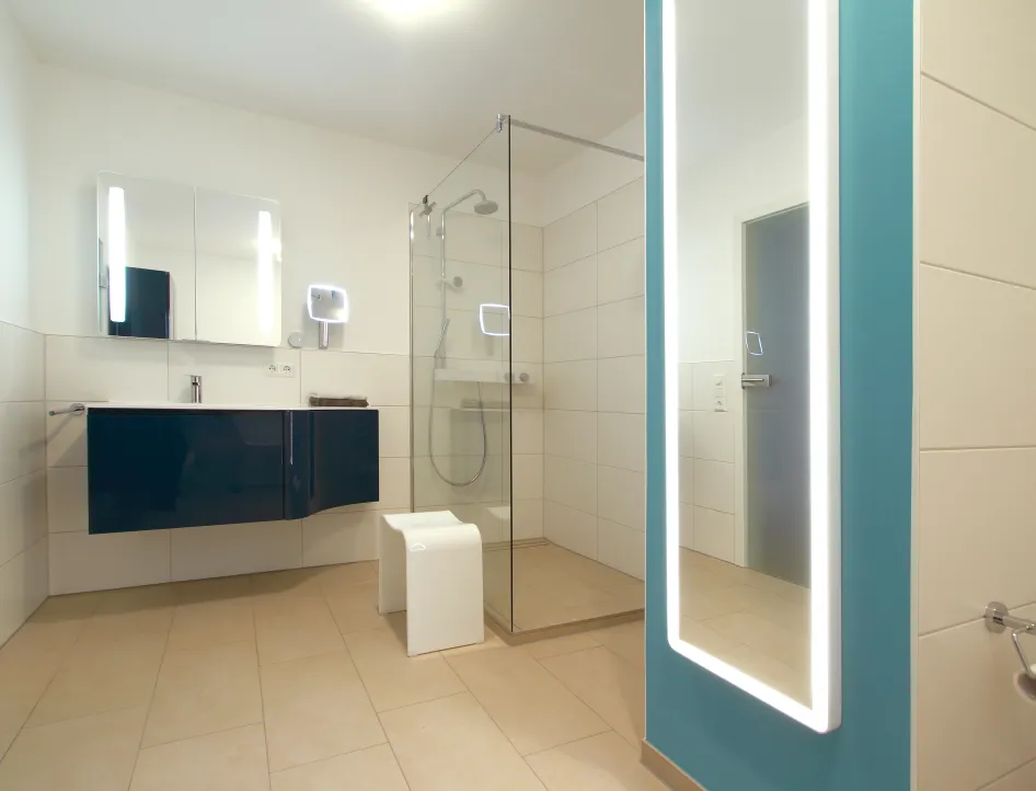 Modernes Badezimmer mit bodengleicher Dusche, wandhängendem Waschtisch und beleuchtetem Ganzkörperspiegel, in einem klaren, minimalistischen Design mit farblichem Akzent.