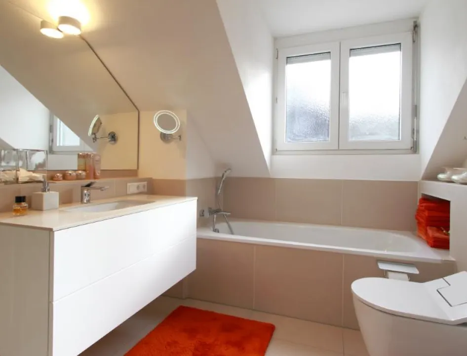 Ein modernes Badezimmer unter einer Dachschräge mit beige-weißen Fliesen und einer hellen, freundlichen Gestaltung.
