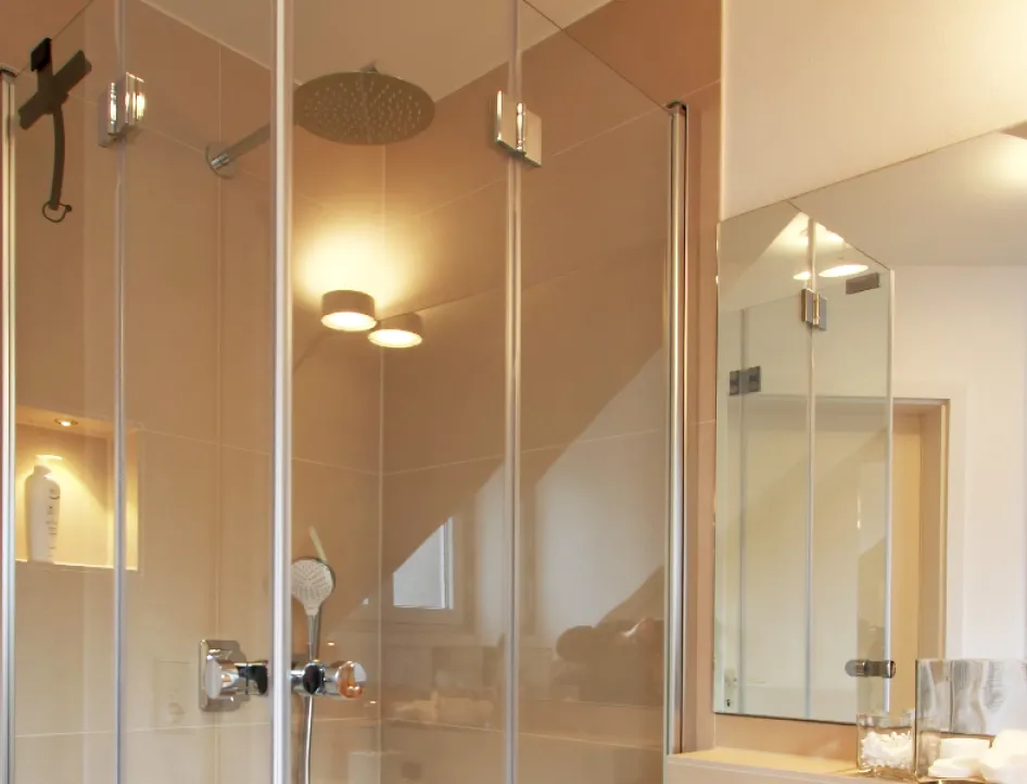 Eine luxuriöse Dusche mit rahmenlosen Glaswänden, die von beigen Fliesen und modernem Design umgeben ist. 