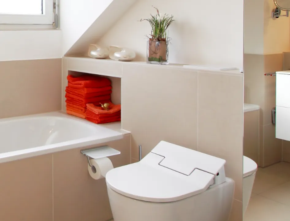 Ein modernes Badezimmer mit einer weißen Badewanne, einer Toilette mit minimalistischem Design und beigefarbenen Wänden.